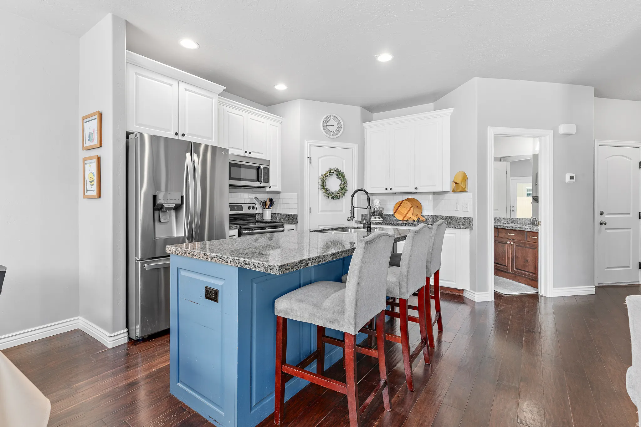 Kitchen featuring a blue-paneled island with seating, granite countertops, white cabinetry, stainless steel appliances, and dark wood-finish flooring