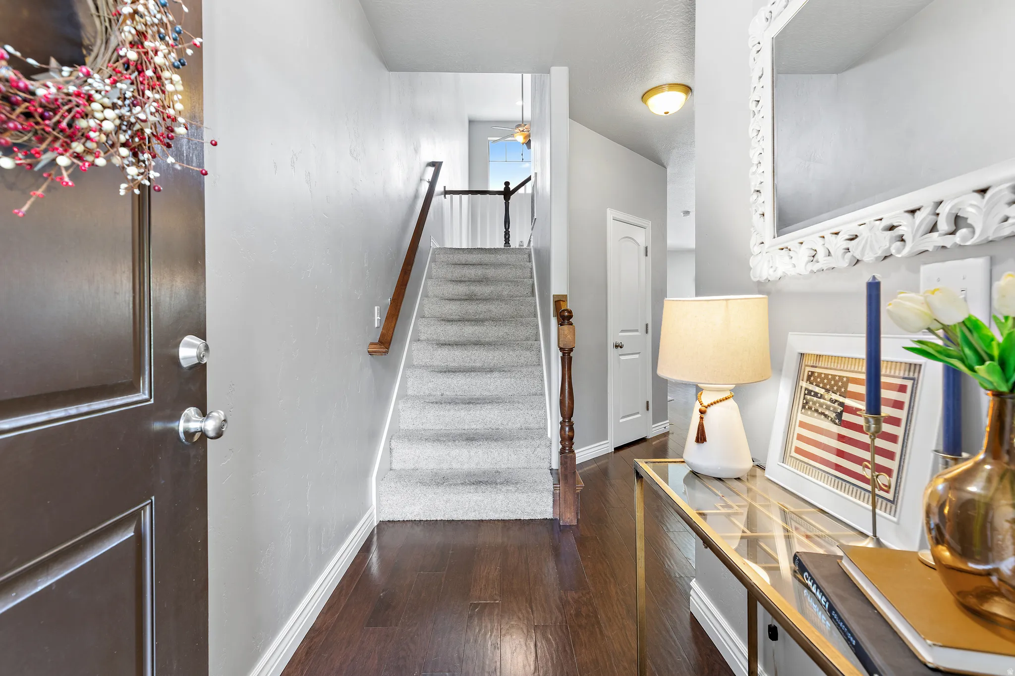 Entryway featuring dark wood-finish flooring, a carpeted staircase with a wood handrail, light gray wall paint, white baseboards, and overhead lighting
