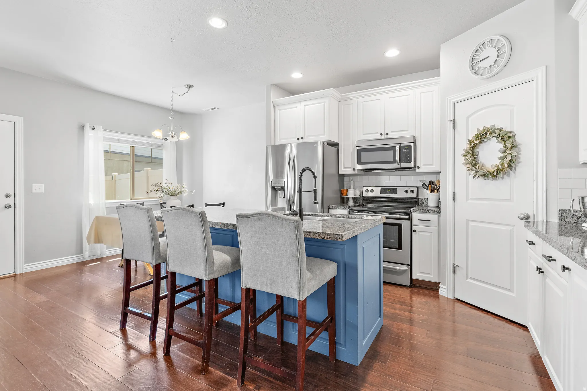 Kitchen featuring a blue-paneled island with granite countertop, stainless steel appliances, white subway tile backsplash, and wood-finish flooring