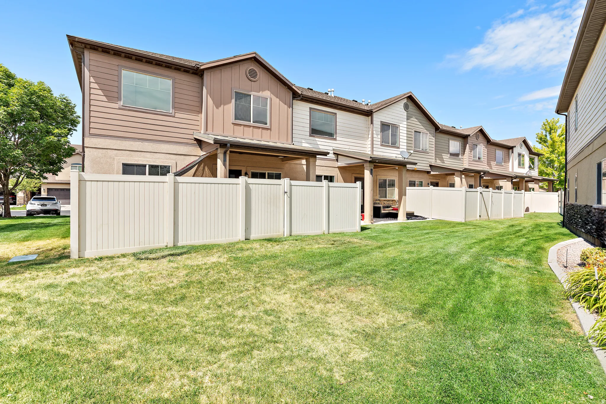Expansive grassy area featuring a vinyl fence, established landscaping, and covered patios