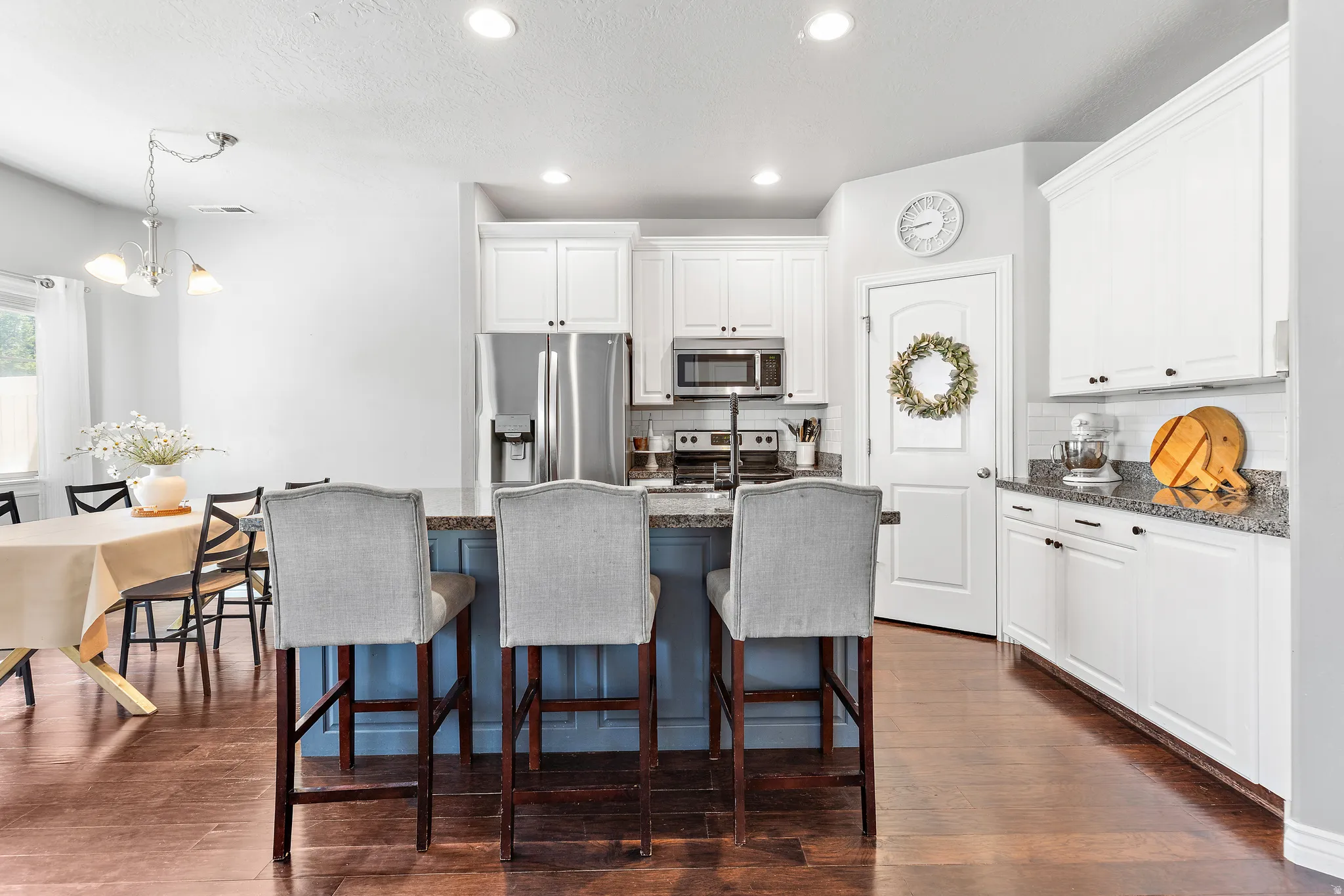 Kitchen featuring an island with seating, white cabinetry, stainless steel appliances, and wood-finish flooring