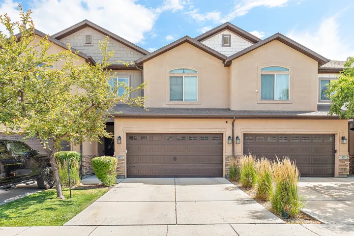 Multi-level stucco exterior featuring two attached garages with paneled doors, stone accents, and decorative outdoor lighting