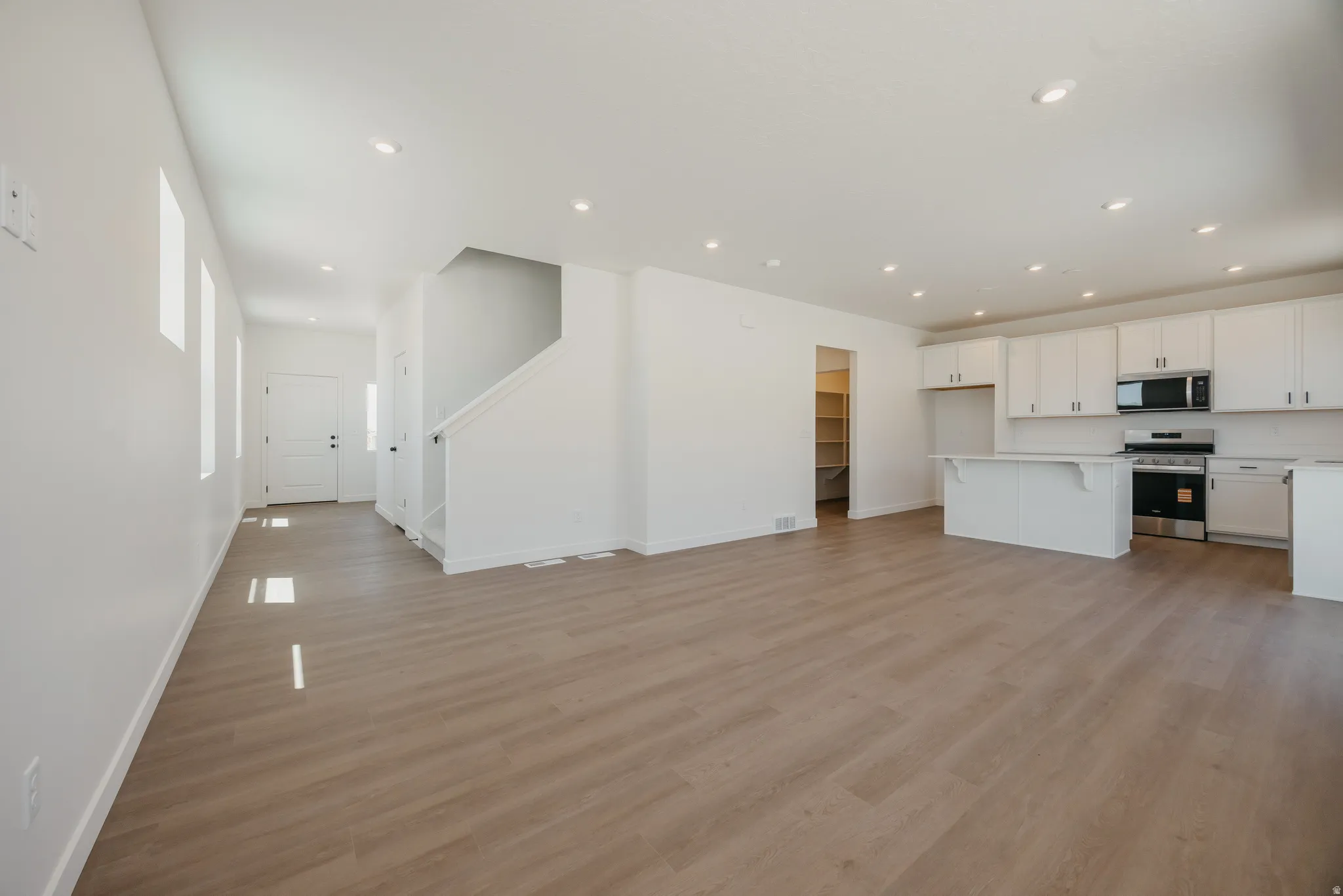 Open-concept living area featuring wood-finish flooring, recessed lighting, a modern kitchen with white cabinetry, a kitchen island, and stainless steel appliances