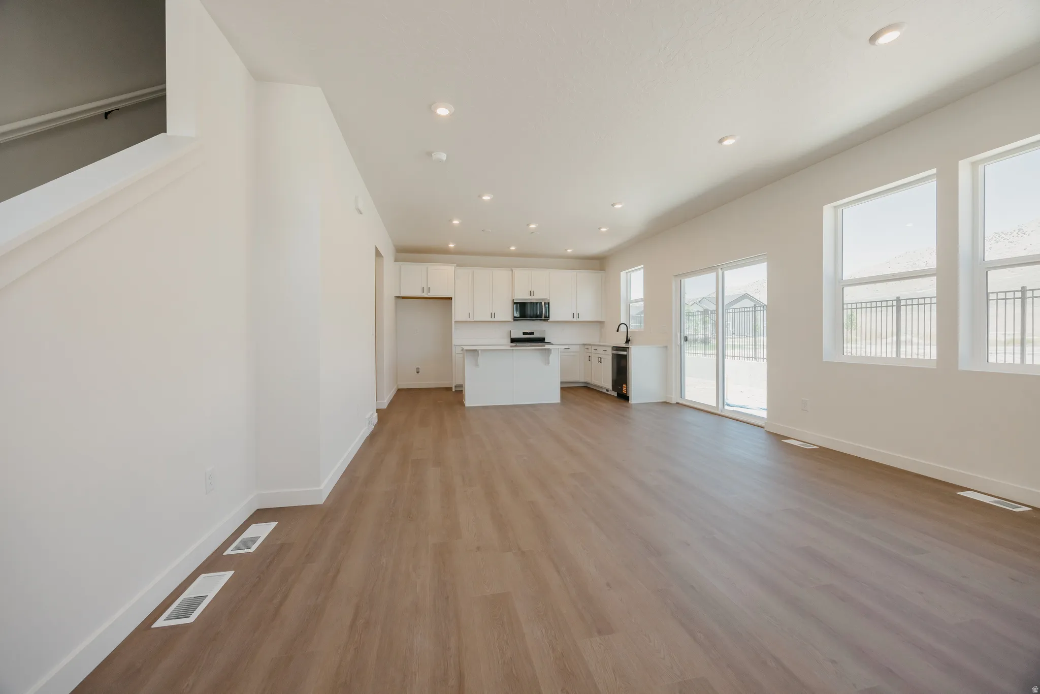 Open-concept living space featuring wood-finish flooring, recessed lighting, and a white kitchen with an island