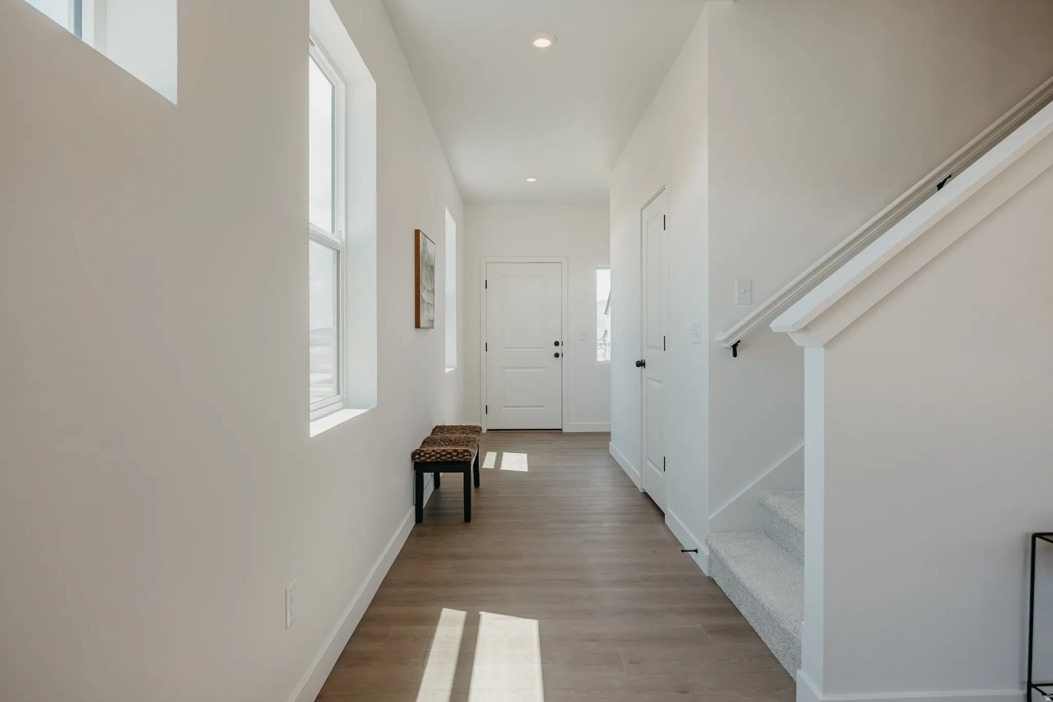 Hallway featuring wood-finish flooring, recessed lighting, and bright white walls
