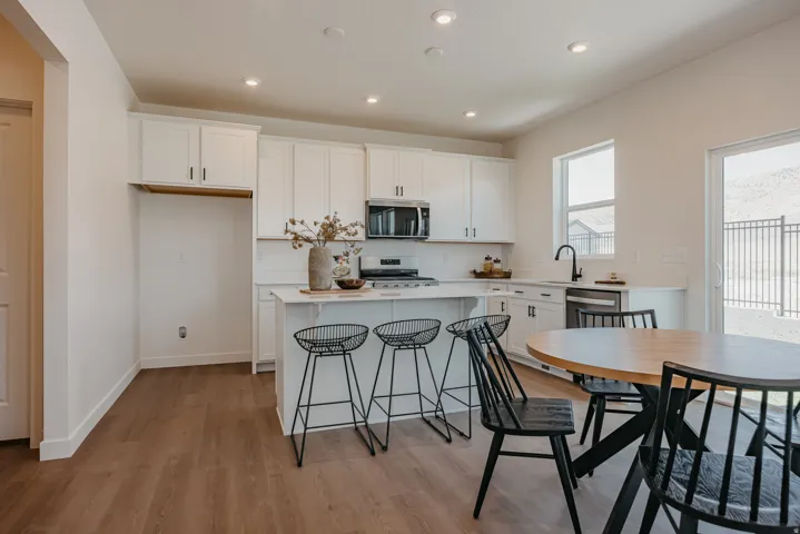 Modern kitchen featuring white cabinetry, stainless steel appliances, a center island with countertop seating, wood-finish flooring, and a sliding glass door leading to the exterior