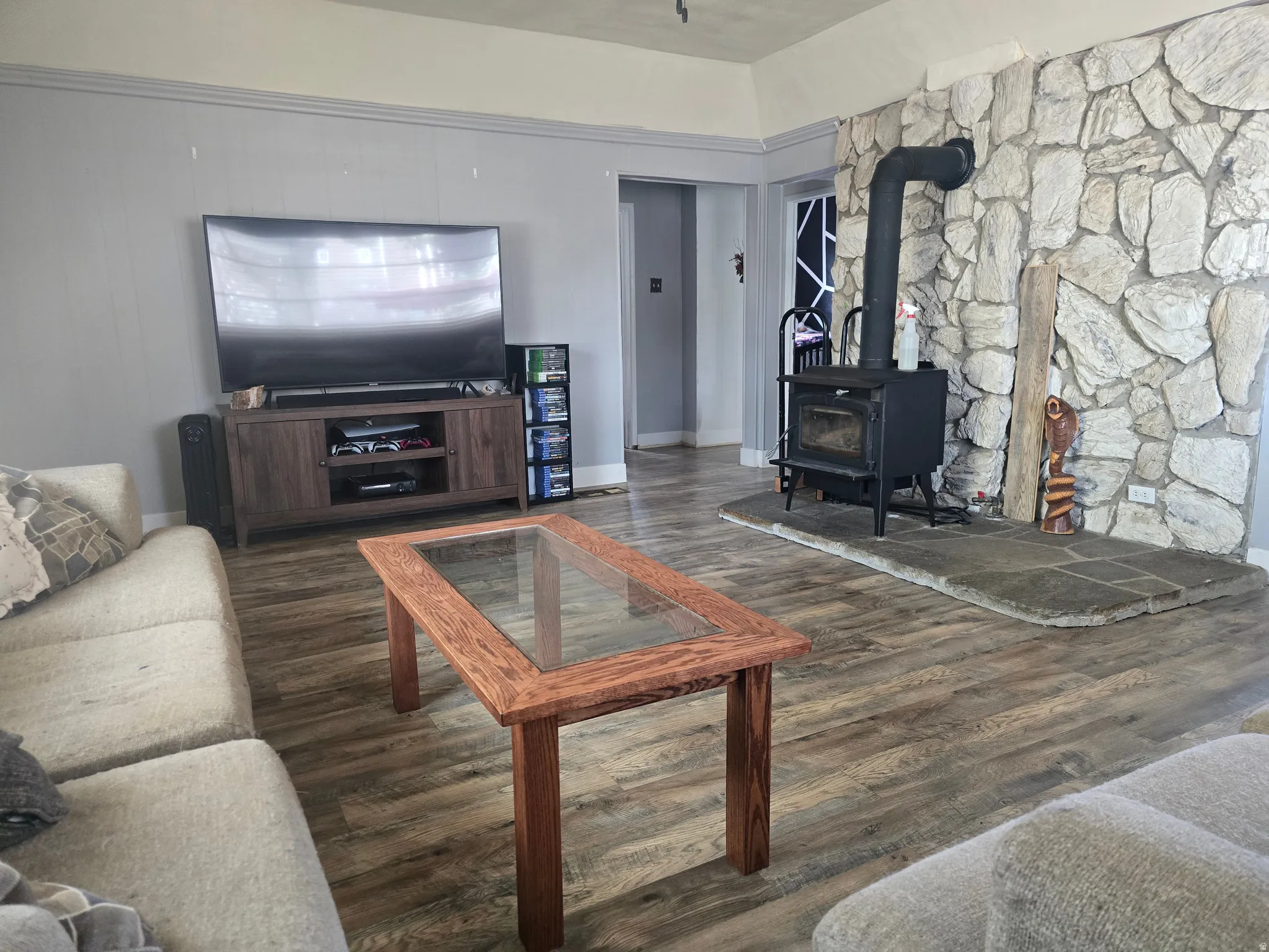 Living area featuring wood-finish flooring, a stone accent wall, and a hearth with a wood-burning stove