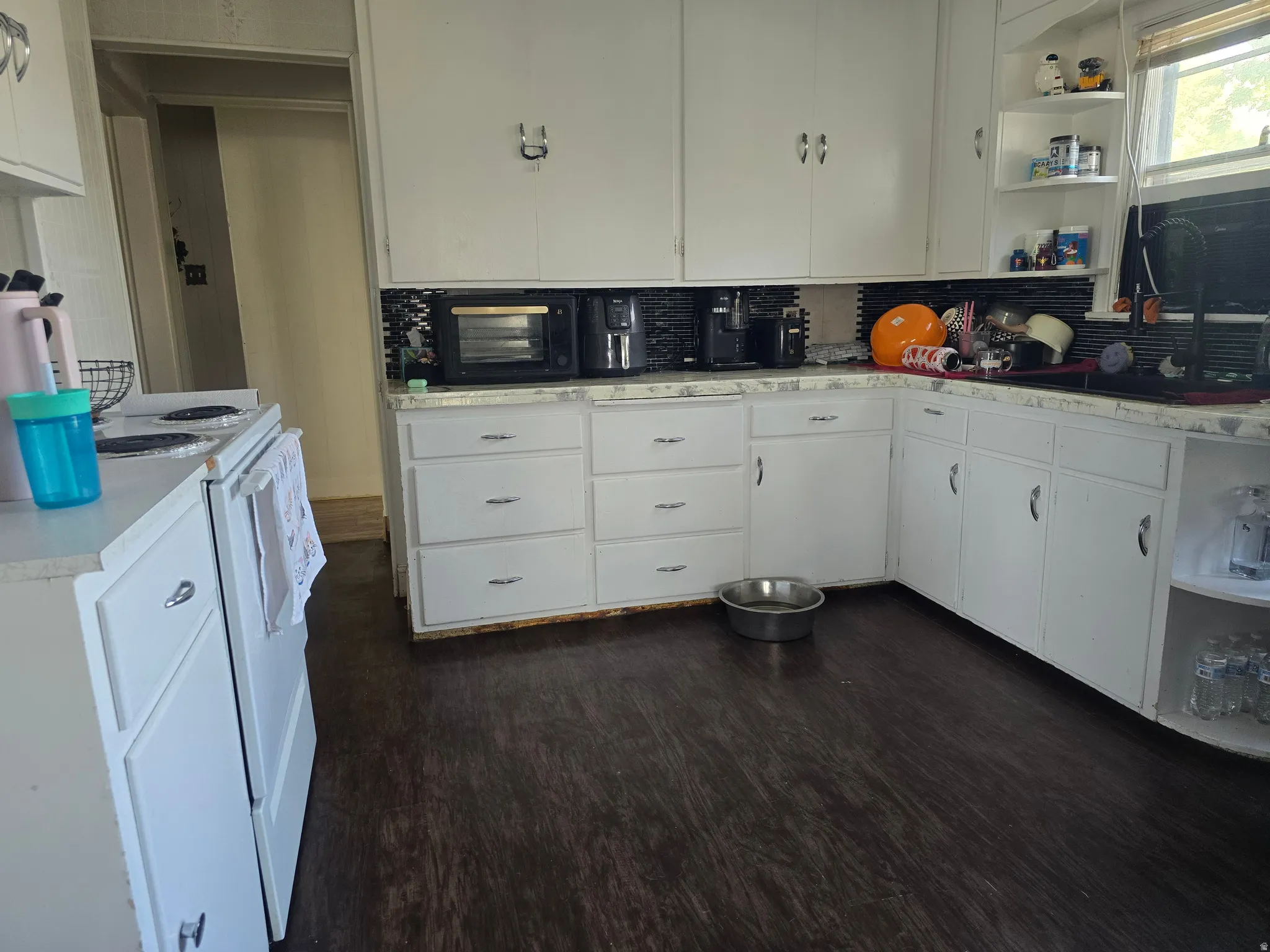 Kitchen featuring abundant white cabinetry, dark wood-finish flooring, a patterned backsplash, corner shelving, and a built-in sink