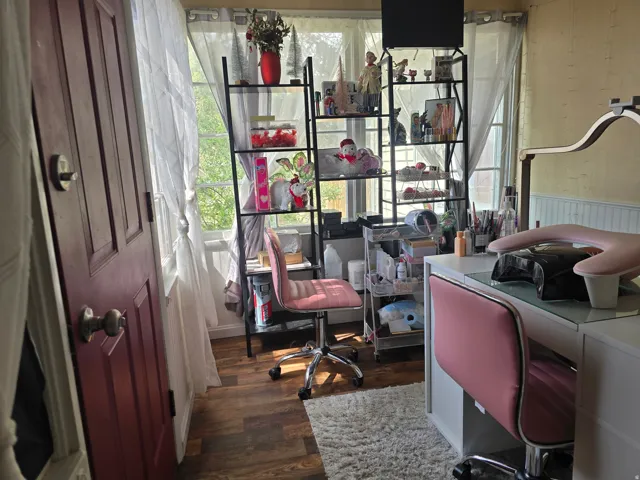 Sunlit interior space featuring wood-finish flooring, multiple windows with white sheer coverings, and a painted paneled door