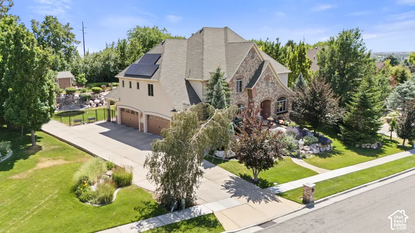 Stone and stucco exterior residence featuring a multi-car garage, solar panels, and a terraced rock garden