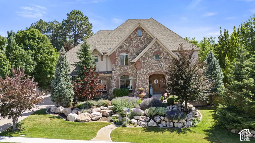 Stone and stucco exterior residence featuring an arched entry, a pitched roofline, and established landscaping