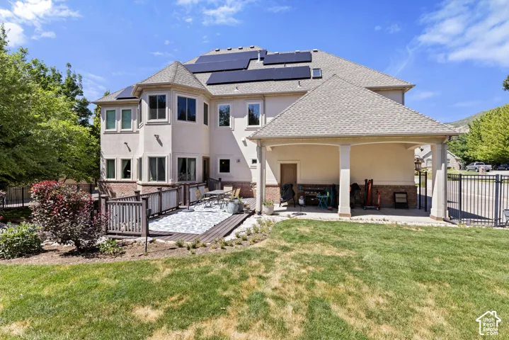 Rear exterior featuring solar panels, a covered patio, an exterior deck with railing, and a stone paver patio