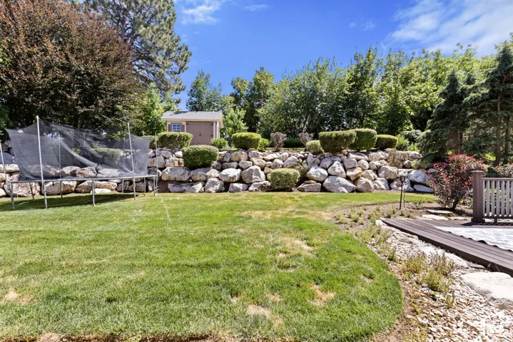 Expansive backyard featuring a lush lawn, a tiered retaining wall crafted from natural stone, and mature landscaping