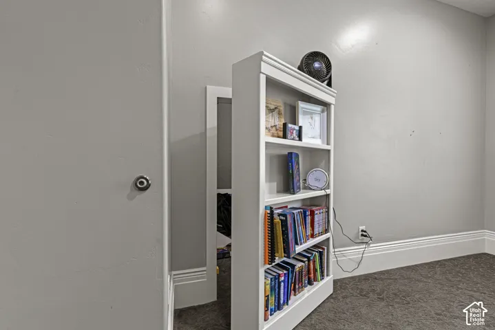 Built-in bookcase concealing a doorway, with light gray wall paint, white baseboards, and gray carpet flooring