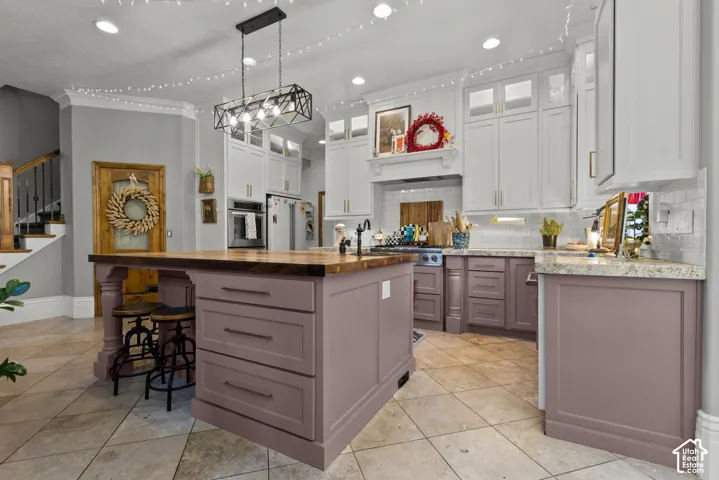 Kitchen featuring an expansive island with wood-finish countertop, dual-tone cabinetry, built-in wall oven, and ceramic tile flooring