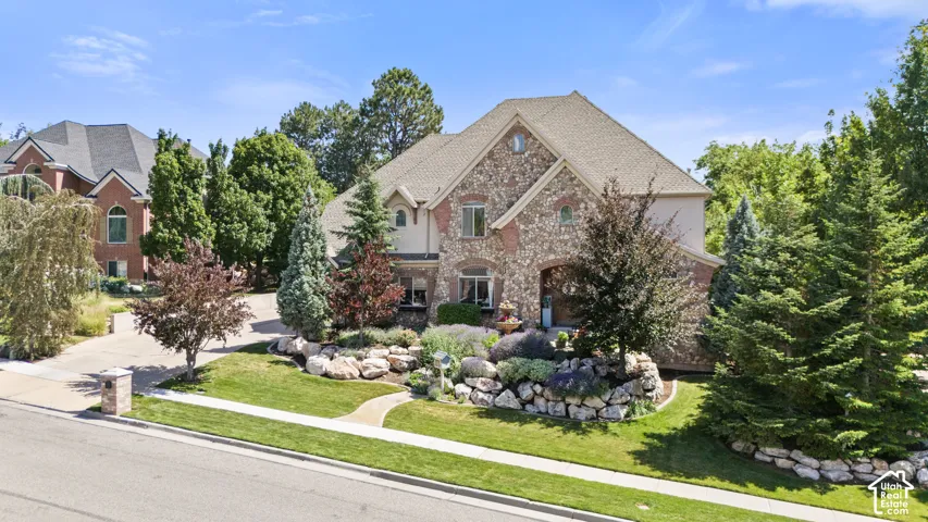 Stone and stucco exterior residence featuring a covered entry, gabled rooflines, a stone-lined planter, and mature landscaping