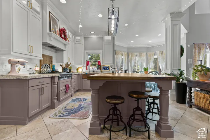 Gourmet kitchen featuring a large central island with a wood countertop, two-tone cabinetry with gold-toned hardware, stainless steel range, light-toned tile flooring, and recessed lighting