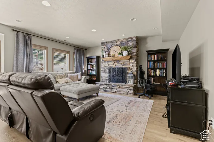 Spacious living area featuring a floor-to-ceiling stone fireplace with a wood mantle, recessed lighting, and light wood-finish flooring