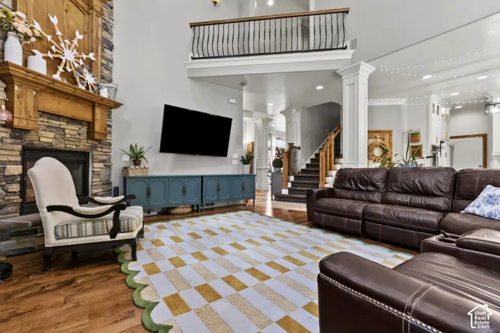 Stone-clad fireplace with a substantial wood mantel, soaring ceilings, wood-finish flooring, a grand staircase, and an upper-level balcony with iron railings