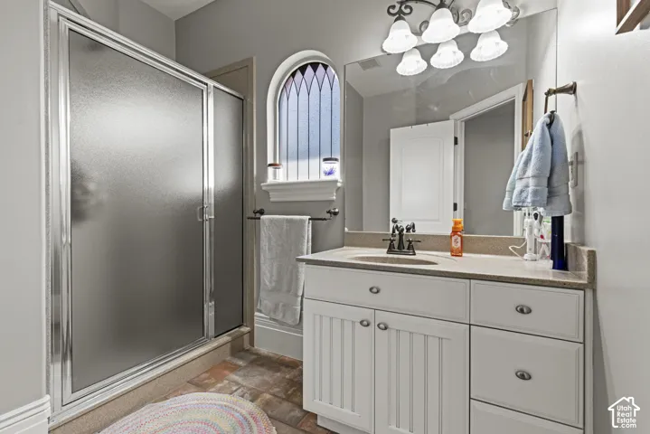Frosted glass shower enclosure with chrome framing, featuring an arched stained glass window, a vanity with a light-toned countertop, beadboard cabinetry, and bronze-finish hardware