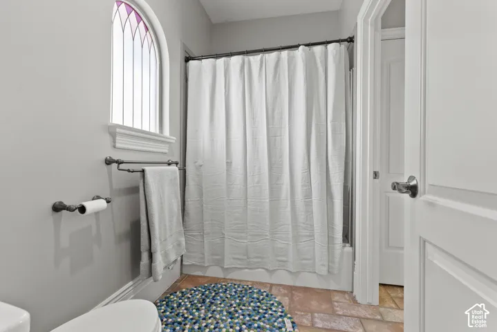 Bathroom featuring an arched window with decorative glass, a shower/tub combination, and terra cotta-style floor tiles