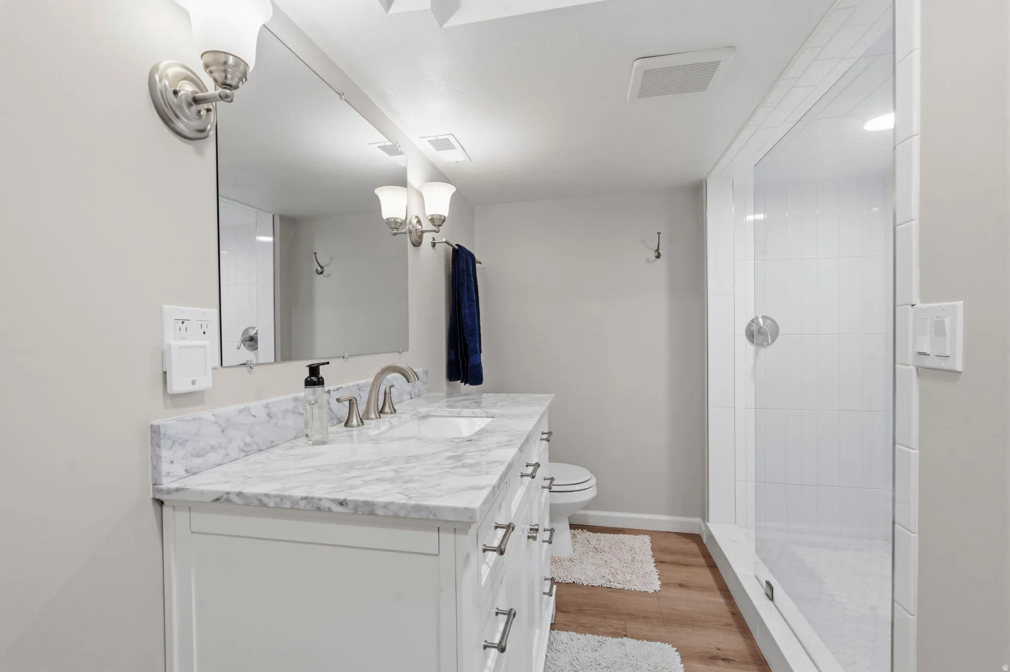 Bathroom featuring a white vanity with soft close doors and drawers, marble countertop with undermount sink,  brushed nickel fixtures, subway tiled walls with glass-enclosed shower and built-in niche, and LVP flooring
