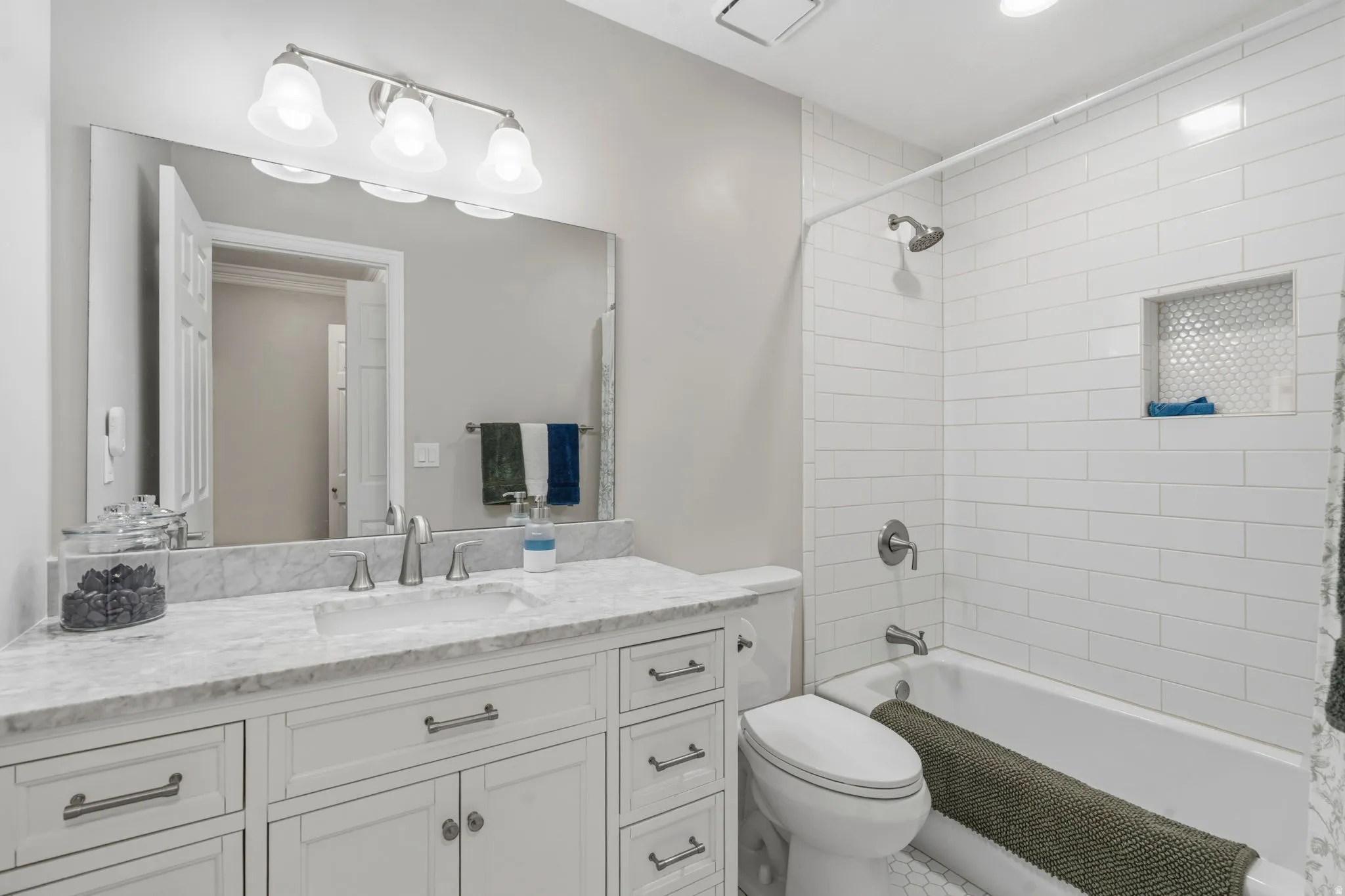 Bathroom featuring a white vanity with soft close doors and drawers, marble  countertop with undermount sink, and brushed nickel fixtures, subway tile bathtub surround and honeycomb niche and tile floor