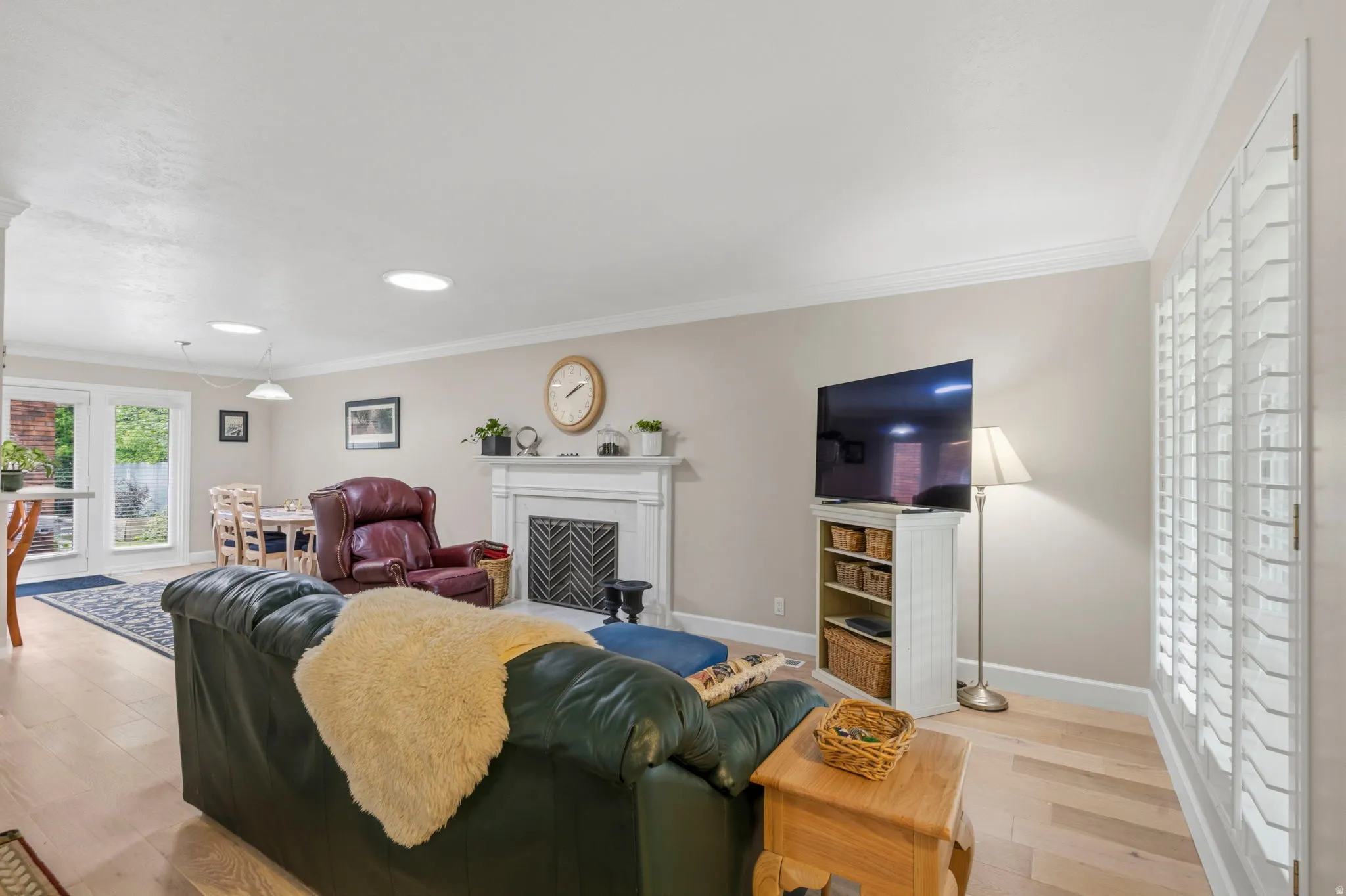 Spacious living area featuring white oak flooring, two-tone paint, solar tubes, lots of natural light, gas log fireplace, plantation shutters, and crown molding