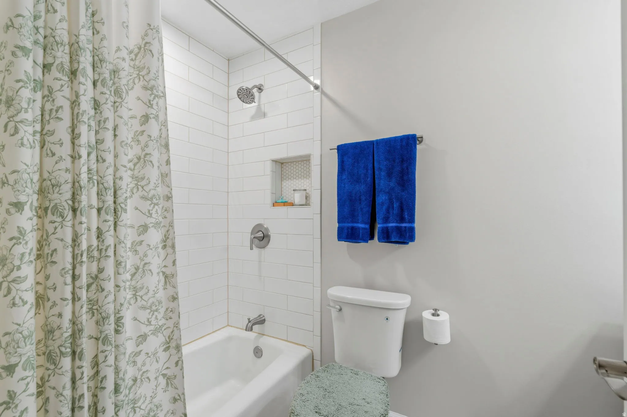 Bathroom featuring subway tile shower surround, built-in shower niche with honeycomb tile accent, and a white bathtub with brushed nickel fixtures