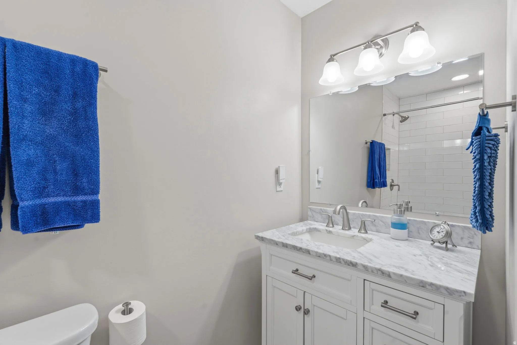 Bathroom featuring a white vanity with soft-close doors and drawers, marble  countertop with undermount sink, and brushed nickel fixtures, honeycomb tile floor