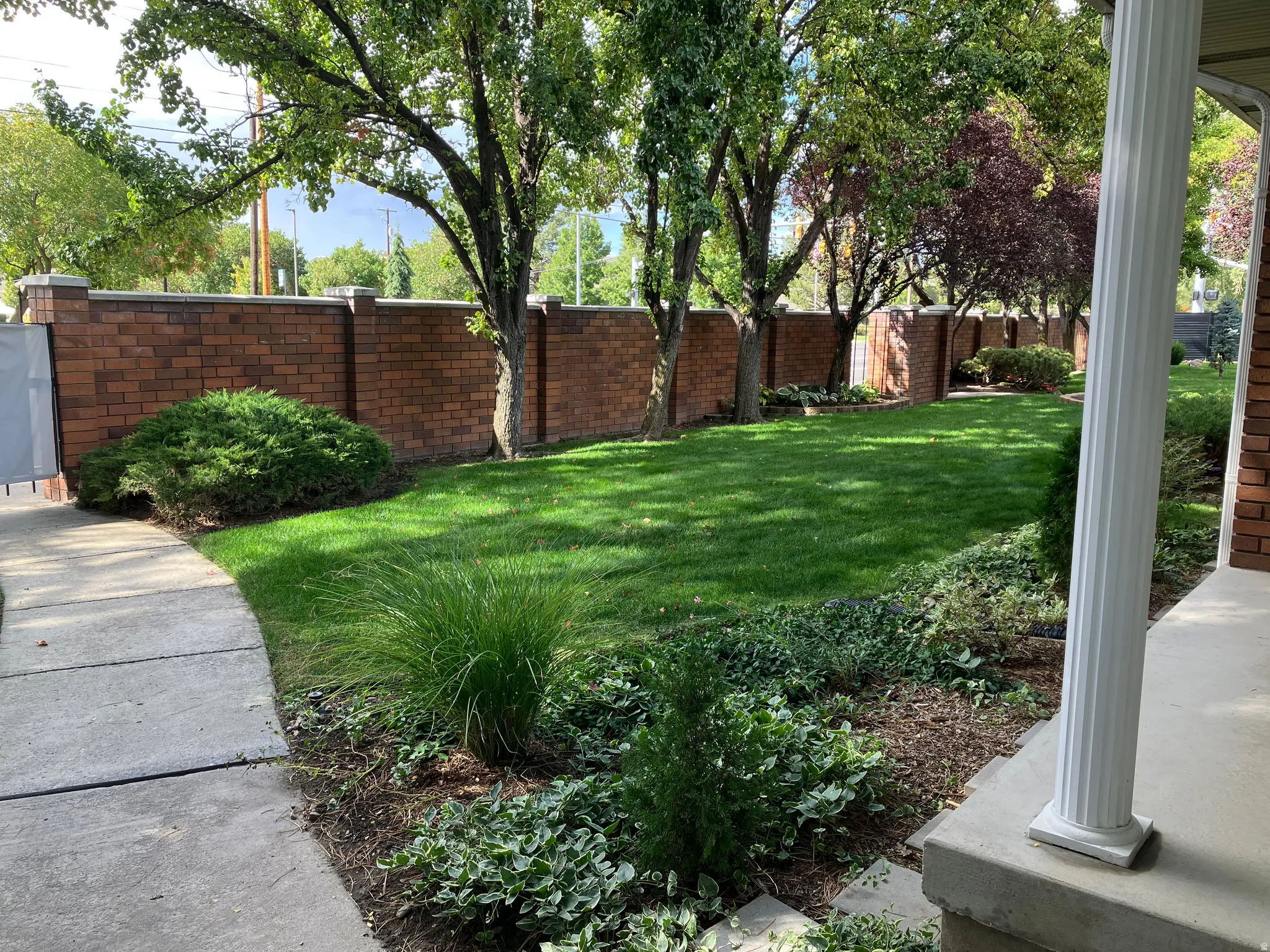 Manicured lawn area with mature trees and a brick privacy wall