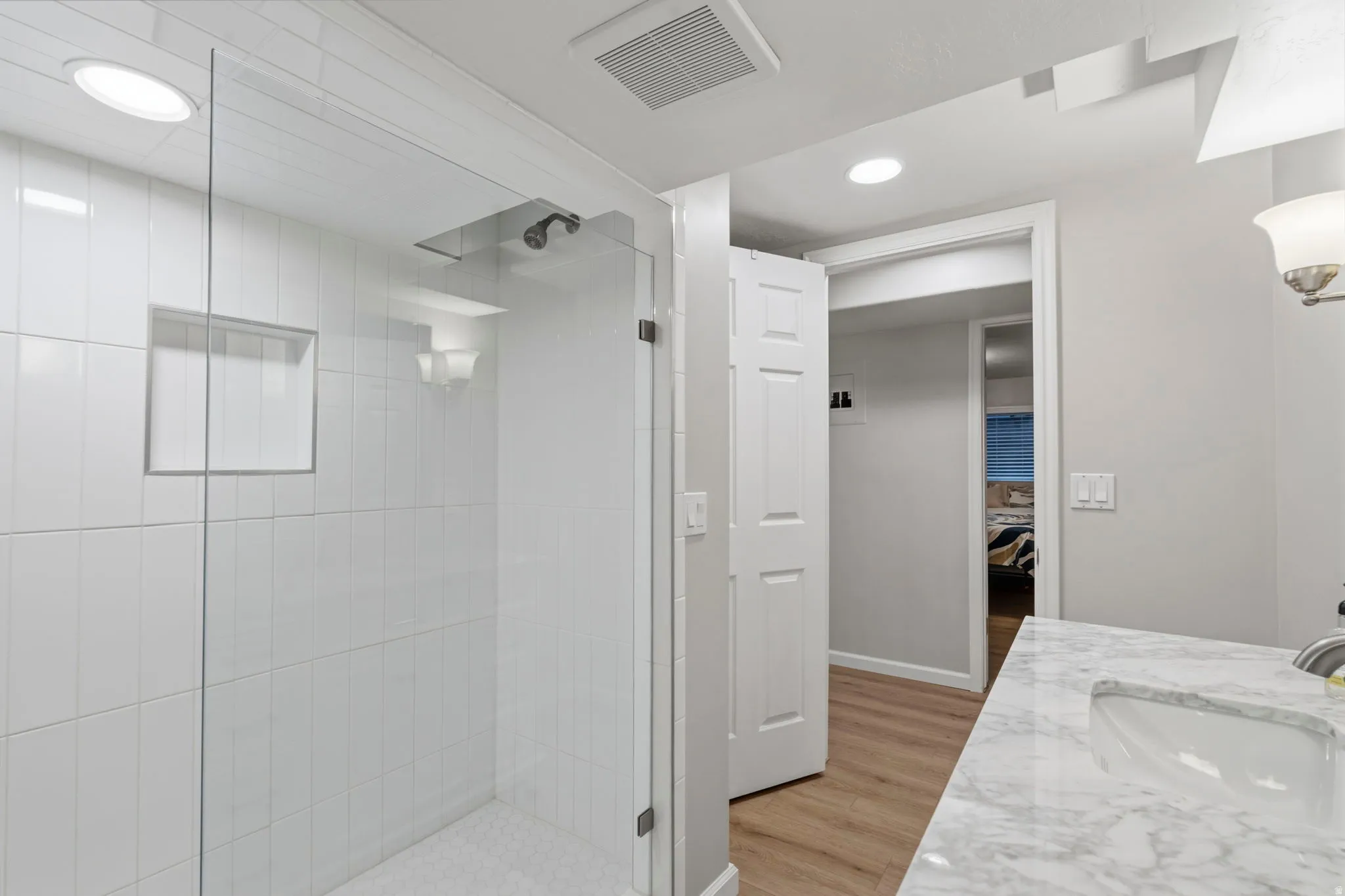 Bathroom featuring a white vanity with soft close doors and drawers, marble countertop with undermount sink, brushed nickel fixtures, subway tiled walls with glass-enclosed shower and built-in niche, and LVP flooring