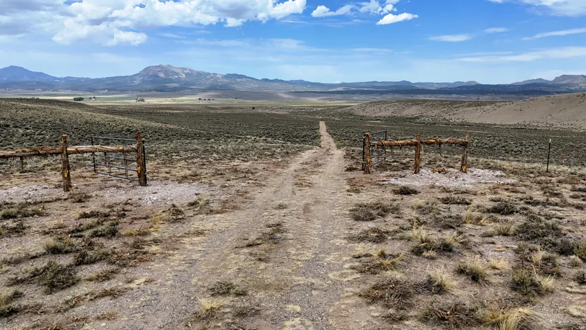 Expansive open land featuring a dirt road leading to a rustic wooden gate