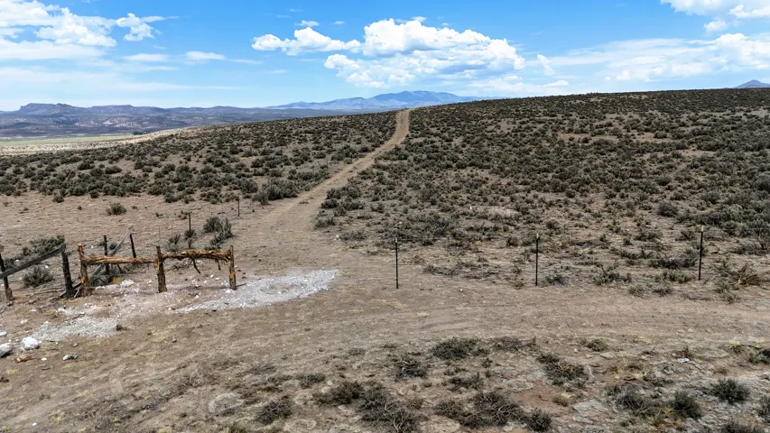 Expansive open land featuring a dirt track, sparse vegetation, and distant mountains under a blue sky