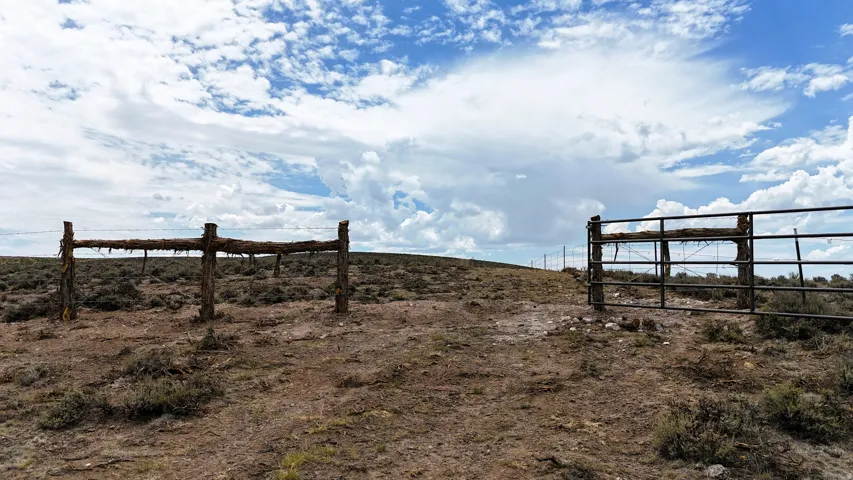 Expansive open land featuring a metal gate entrance and a rustic wooden fence