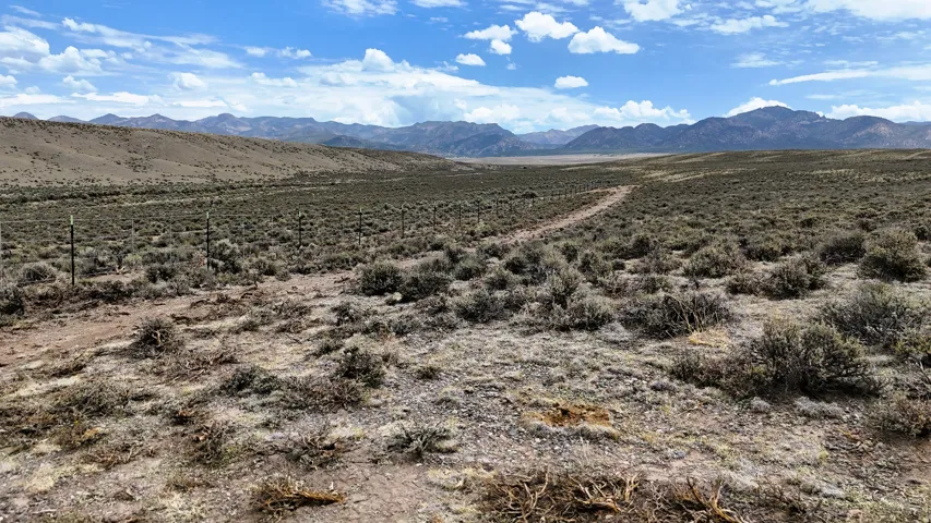 Expansive undeveloped land featuring a natural landscape, distant mountain ranges, a clear blue sky, and a visible dirt path