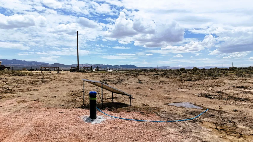 Expansive undeveloped land featuring a water well with a blue cap, a solar panel array, and distant mountain scenery