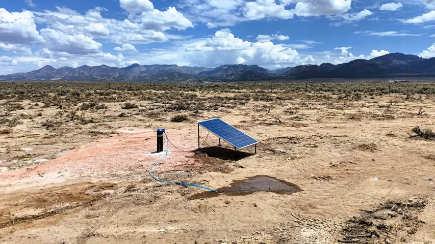 Solar panel array powering a wellhead system in a vast, open landscape with distant mountains