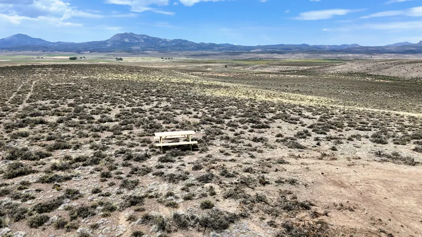 Expansive undeveloped land featuring a rustic picnic table, low-lying scrub brush, and distant mountains