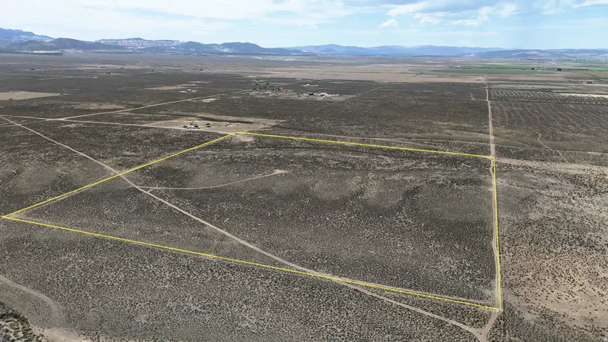 Expansive undeveloped land featuring natural arid vegetation, multiple unpaved access paths, and distant mountain ranges