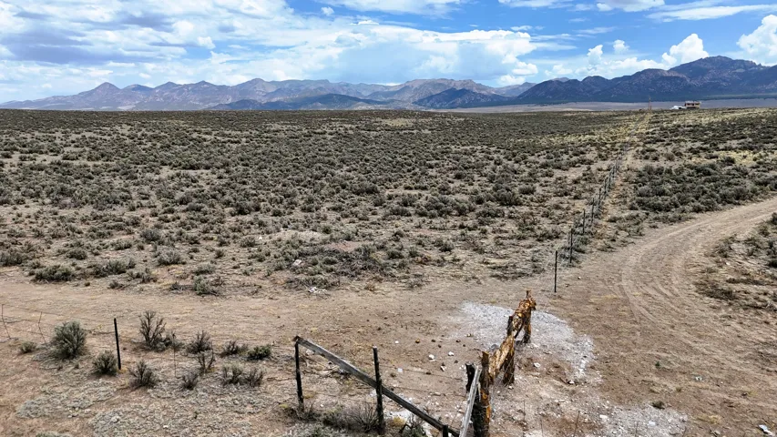 Expansive undeveloped land with a distant mountain backdrop, featuring natural scrub brush, a partial wire fence, and a dirt path