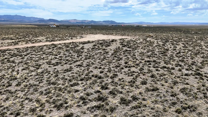 Expansive desert landscape featuring natural scrub vegetation and distant mountain ranges under a partly cloudy sky