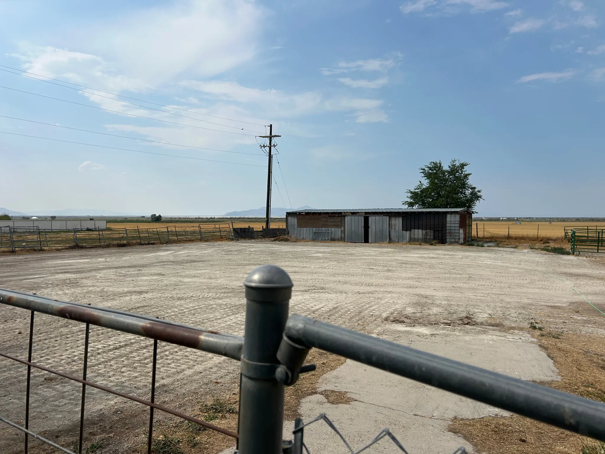 Gated entry to an expansive, unpaved lot with a corrugated metal 4 stall Barn