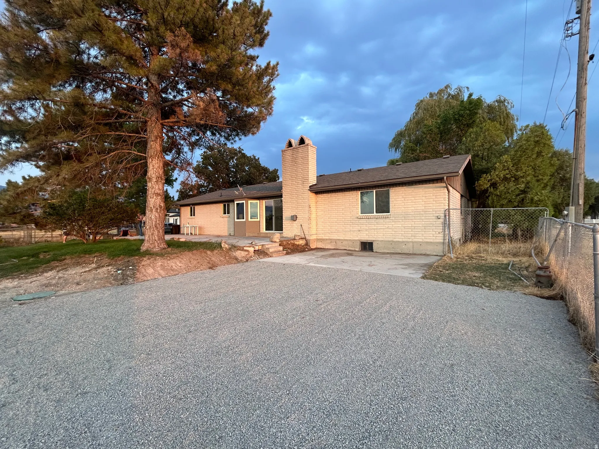 Brick exterior with a prominent chimney, dark shingle roofing, and a gravel driveway