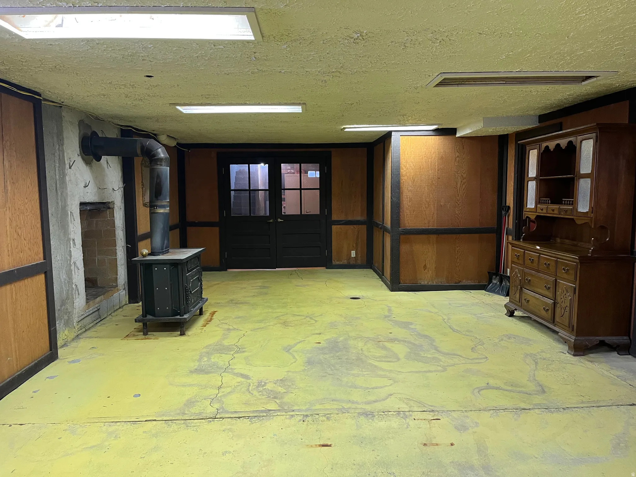 Wood paneling on walls, concrete flooring, recessed lighting, and a wood-burning stove with a brick-lined hearth