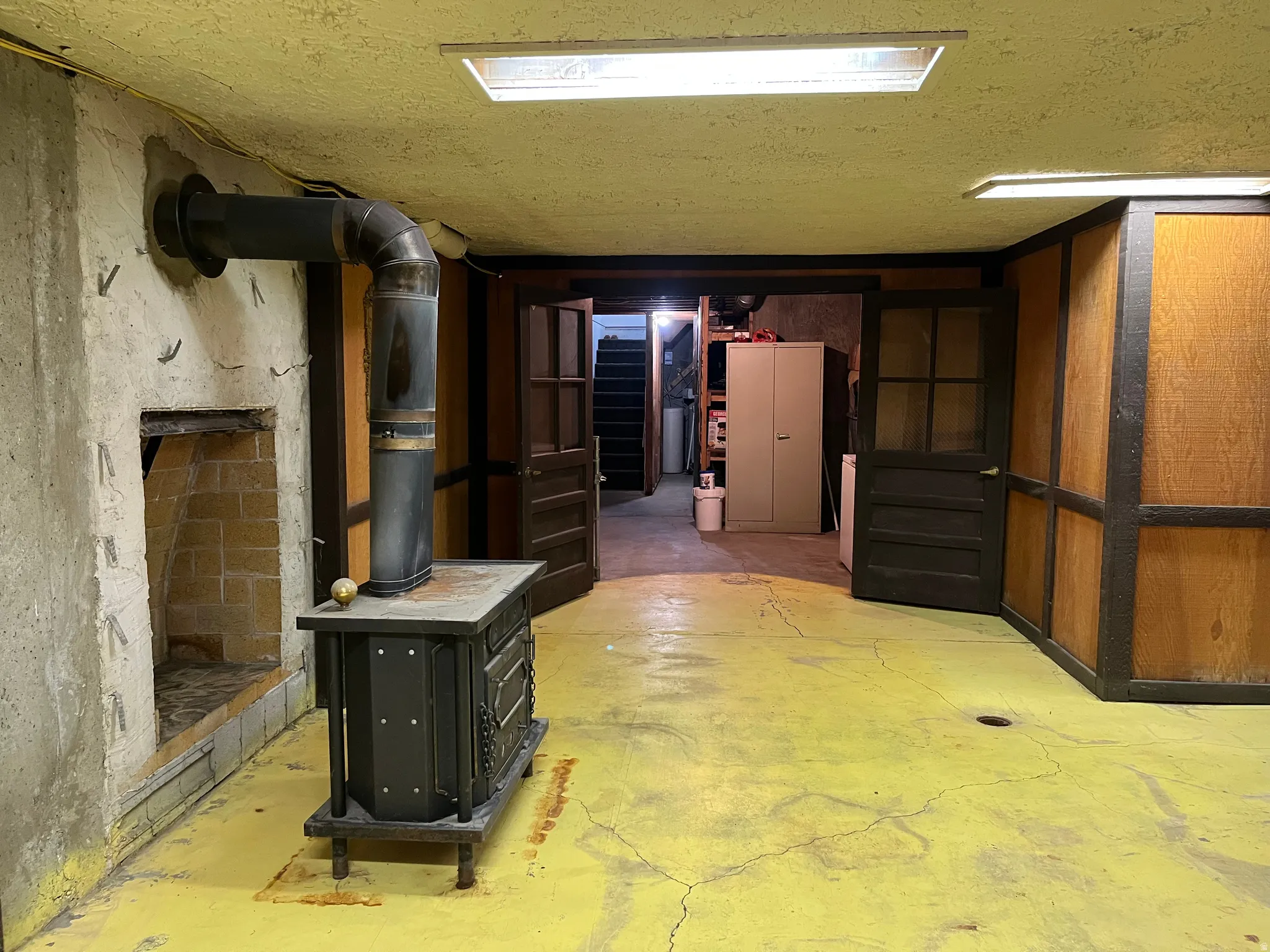 Wood-burning stove with metal flue, brick-lined alcove, and painted concrete flooring