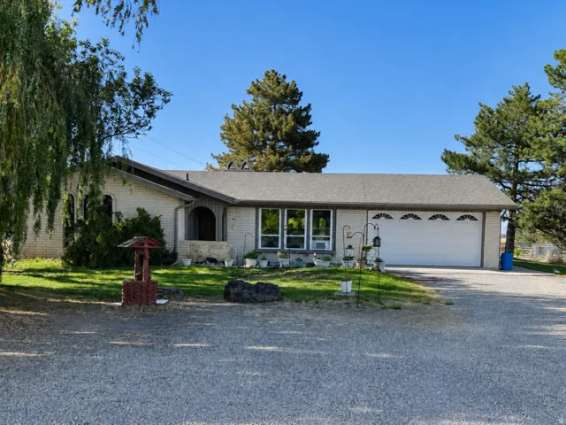 Single-story exterior with a gravel driveway, attached two-car garage, and mature trees surrounding the property