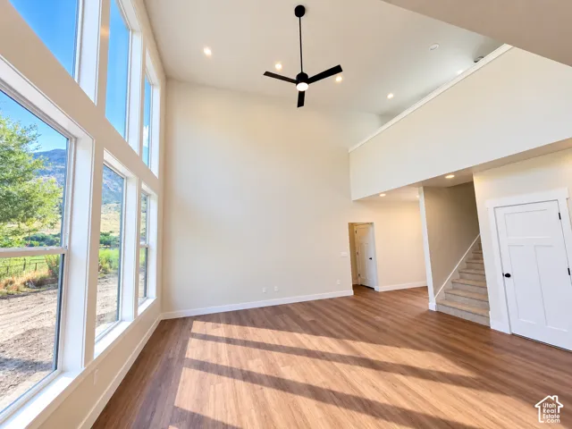 Double-height ceiling with recessed lighting, wood-finish flooring, two-story window wall, and a black ceiling fan