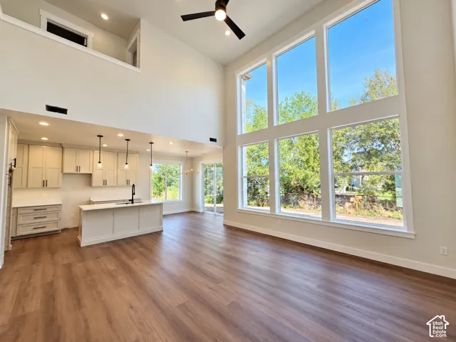 Vaulted ceilings, expansive windows, wood-finish flooring, kitchen island with sink, and recessed lighting