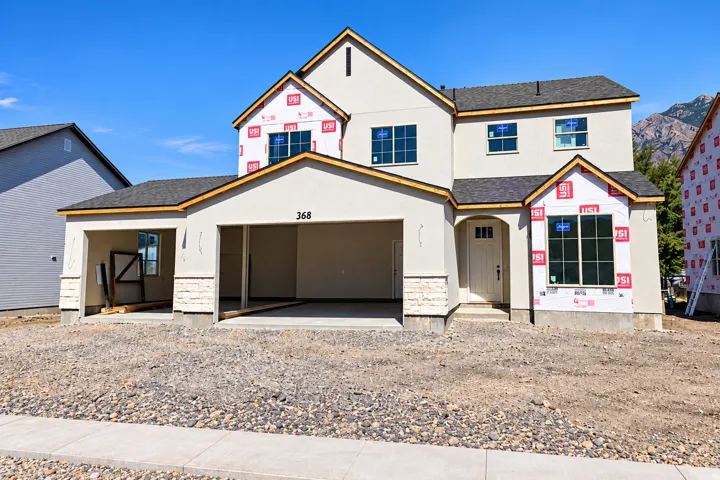 Two-story construction featuring an attached three-car garage, stucco exterior, and a stone veneer foundation accent